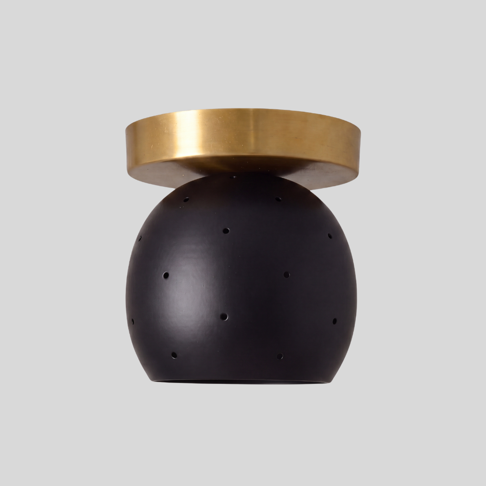 Small flush mount ceiling light with a matte black spherical globe shade and a raw brass circular canopy, featuring pinhole light details in a modern minimalist design.