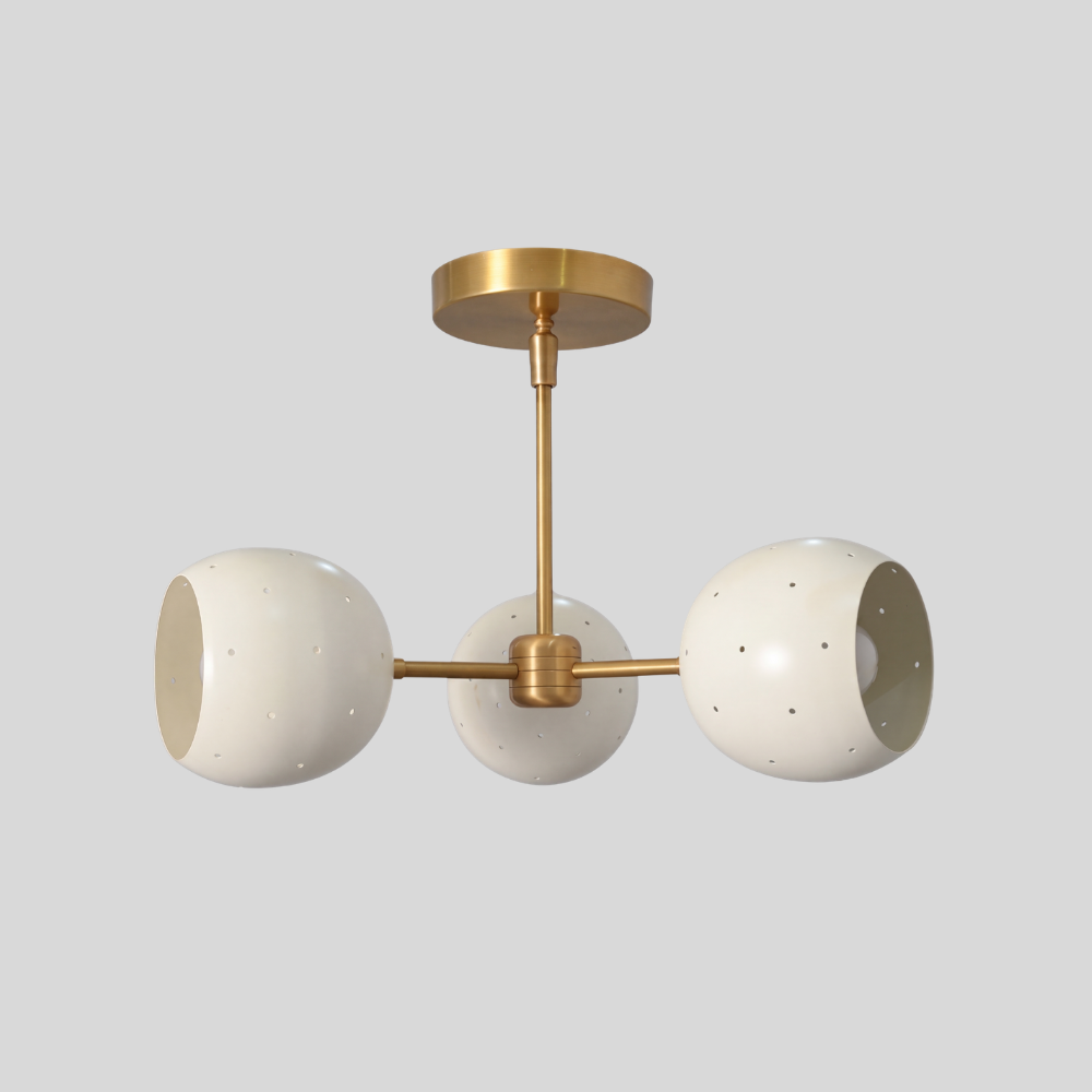 Triple white orb ceiling light featuring three perforated globe shades on a raw brass semi-flush mount, with a mid-century modern aesthetic and ambient pinhole lighting details.