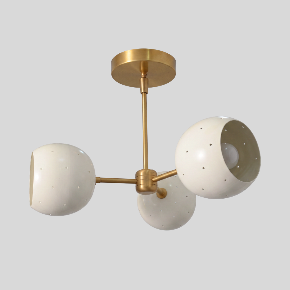 Triple white orb ceiling light featuring three perforated globe shades on a raw brass semi-flush mount, with a mid-century modern aesthetic and ambient pinhole lighting details.