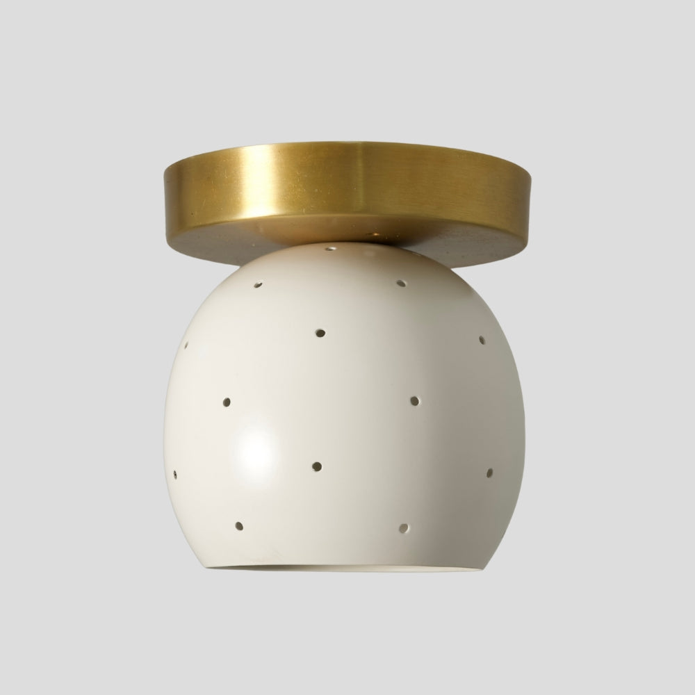 Small flush mount ceiling light with perforated matte white dome shade and raw brass base on a neutral background