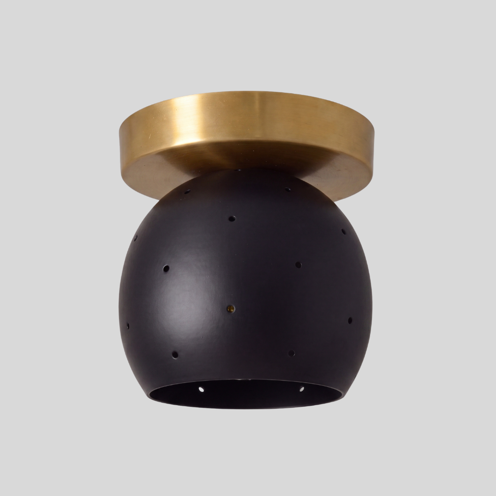 Small flush mount ceiling light with a matte black spherical globe shade and a raw brass circular canopy, featuring pinhole light details in a modern minimalist design.