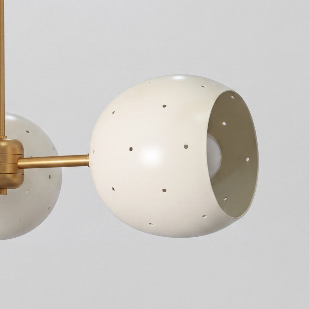 Triple white orb ceiling light featuring three perforated globe shades on a raw brass semi-flush mount, with a mid-century modern aesthetic and ambient pinhole lighting details.